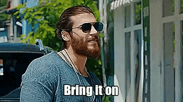 a man with a beard wearing sunglasses and a blue shirt says bring it on