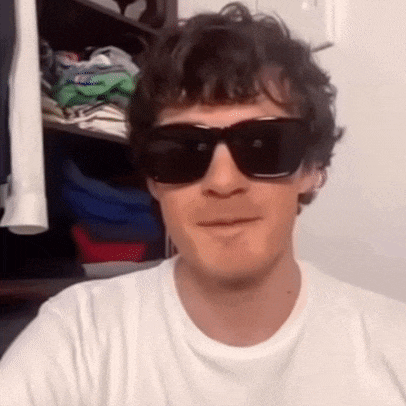 a man wearing sunglasses and a white t-shirt is smiling .
