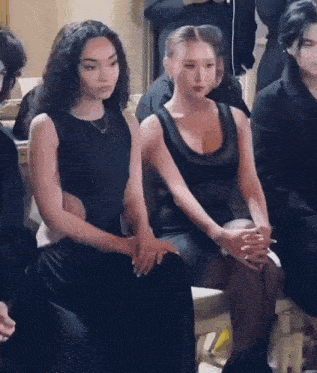 two women in black dresses are sitting next to each other in a crowd .