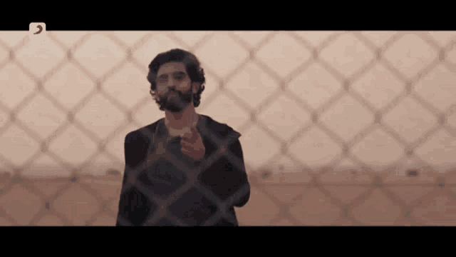 a man is standing in front of a chain link fence and pointing at something