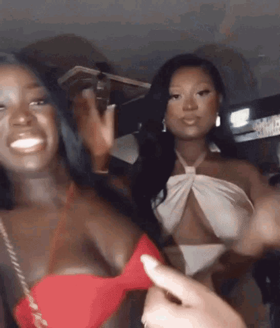 a couple of women are standing next to each other and one of them is wearing a red bikini top .
