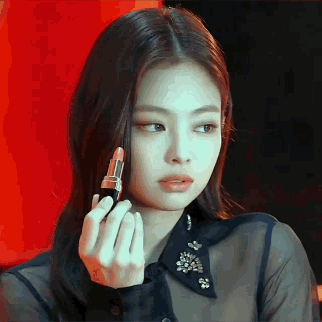 a woman in a black shirt is holding a lipstick in her right hand