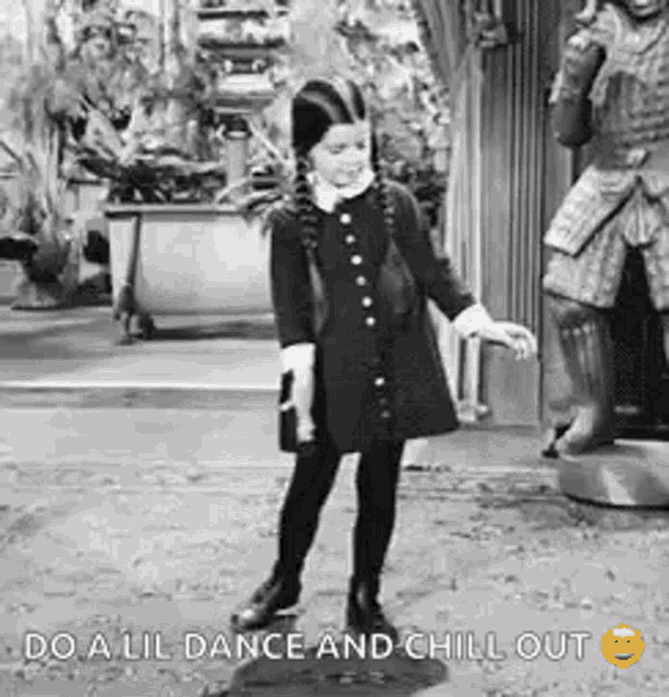 a little girl in a black dress is dancing in front of a statue of a man .