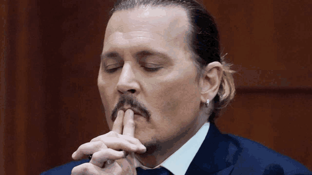 a man with a ponytail and a mustache holds his finger to his mouth