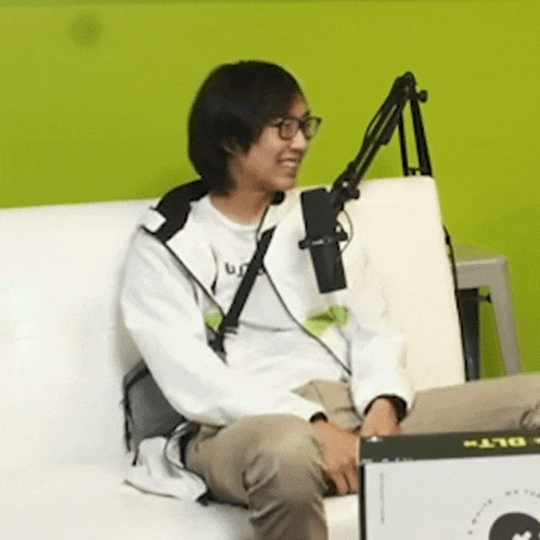 a man wearing glasses is sitting on a couch with a microphone and a box that says " play "