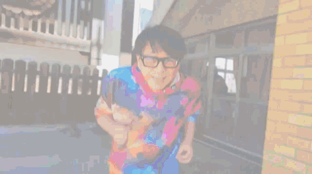 a man wearing glasses and a tie dye shirt is standing in front of a brick wall