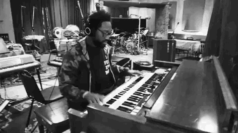 a man wearing headphones is playing an organ in a room with a drum set behind him