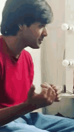 a man in a red shirt is sitting in front of a mirror talking