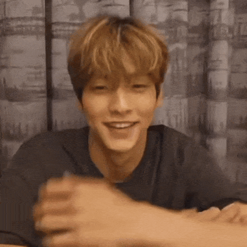 a young man is sitting at a table with his hands folded in front of him and smiling .
