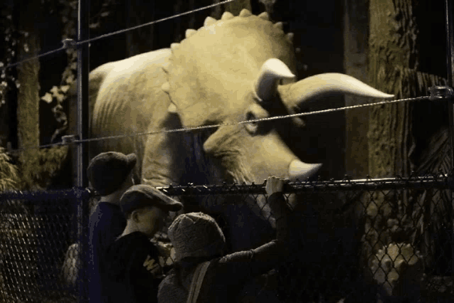 a group of people looking at a dinosaur behind a fence