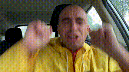a bald man in a yellow jacket is sitting in a car and making a funny face .