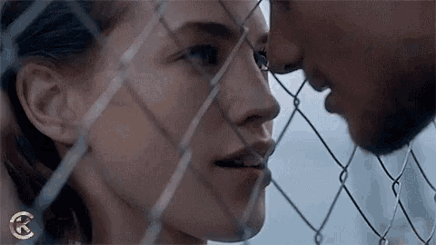 a man and a woman are kissing in front of a chain link fence .