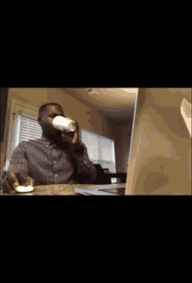 a man is holding a cup in front of a laptop computer