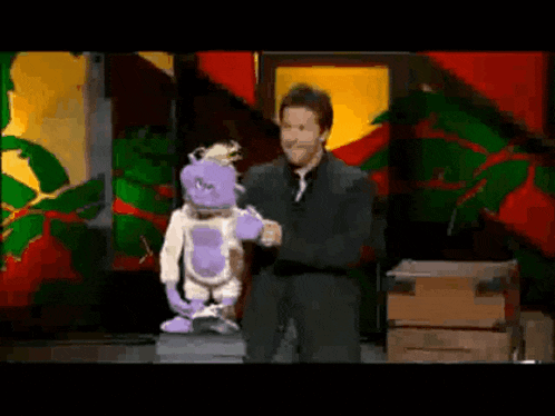 a man in a suit and tie is holding a purple puppet
