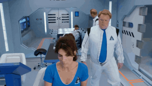 a man in a white suit with the letter a on it walks behind a woman in a blue shirt
