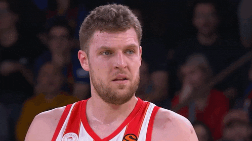 a man with a beard wears a red and white jersey with a hawks logo on it
