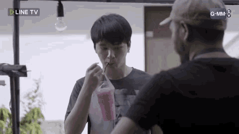 a man is drinking a pink drink with a straw while another man looks on .