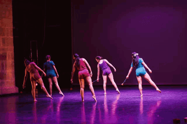 a group of women are dancing on a stage in front of a purple backdrop