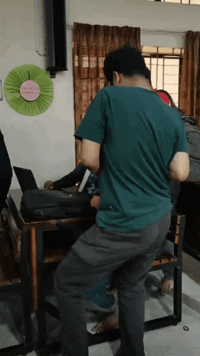 a man in a green shirt is standing in front of a desk with a laptop on it
