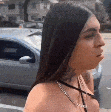 a woman with long hair and a tattoo on her neck is standing in front of a car