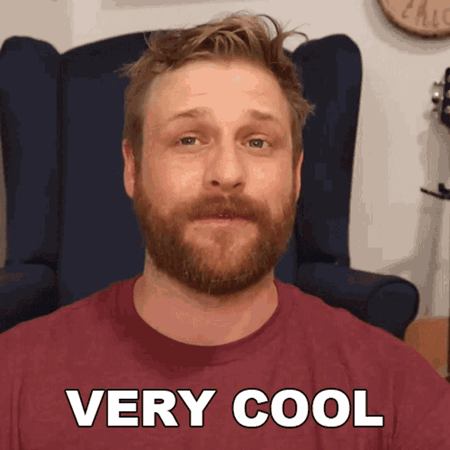 a man with a beard is sitting in a chair and says very cool