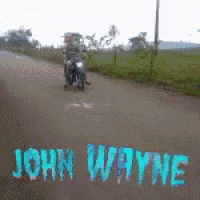 a person riding a motorcycle down a road with the name john wayne written on the side of the road
