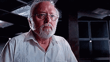 a man with a beard and glasses is standing in a dark room looking at the camera .