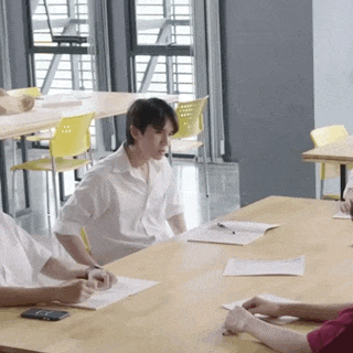 a group of people are sitting around a wooden table with papers on it .
