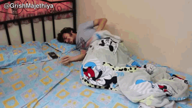 a man laying on a bed with a mickey mouse blanket on it