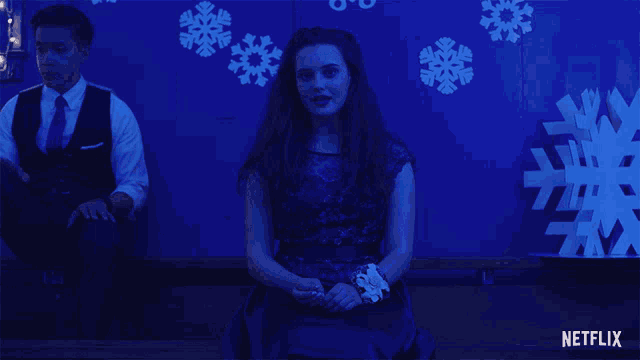 a man and a woman are sitting in front of a blue wall with snowflakes on it and a netflix logo