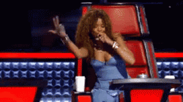 a woman in a blue dress is sitting in a red chair with her arms in the air