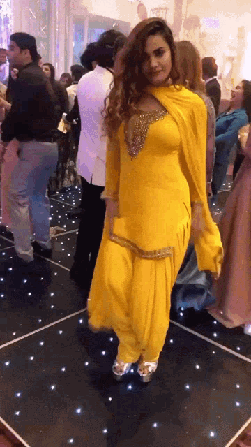 a woman in a yellow dress is dancing on a black dance floor