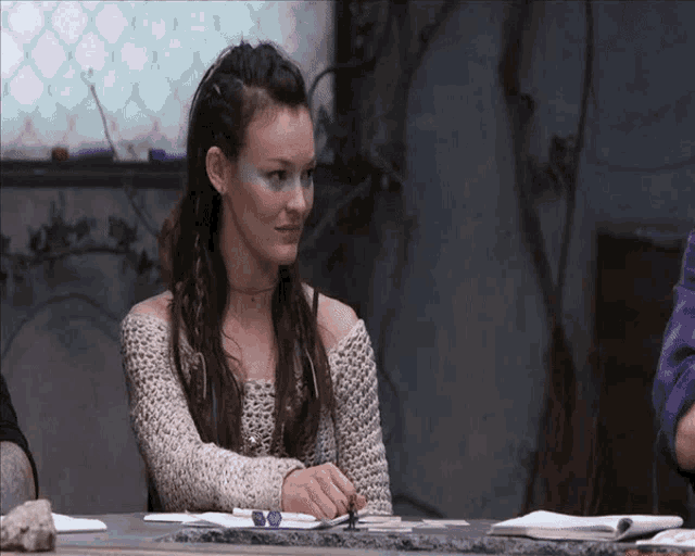 a woman in a knitted sweater sits at a table with a book