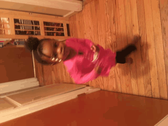 a young girl in a pink shirt is standing on a wooden floor