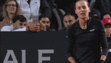 a woman wearing a black ea7 shirt holds a tennis racket