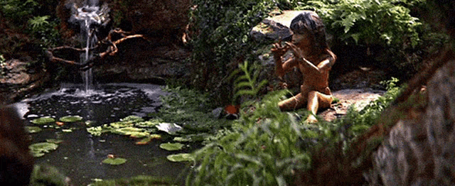 a boy is playing a flute in front of a waterfall