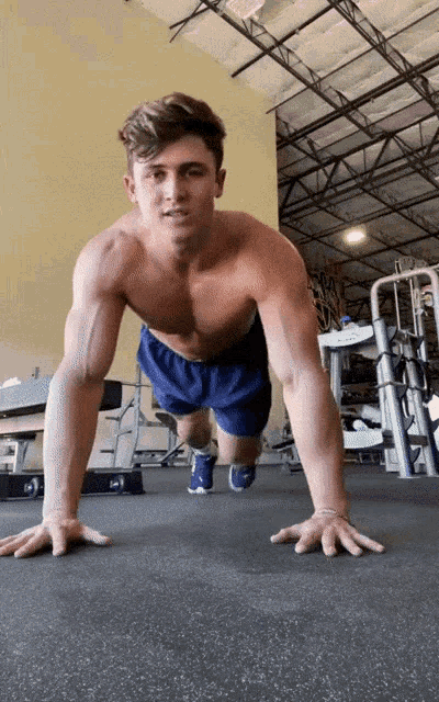 a shirtless man is doing push ups on the floor of a gym