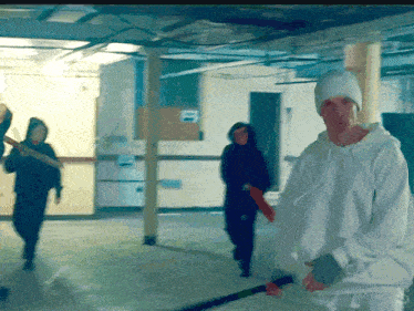 a man in a white hoodie is holding a bat in a room with other people