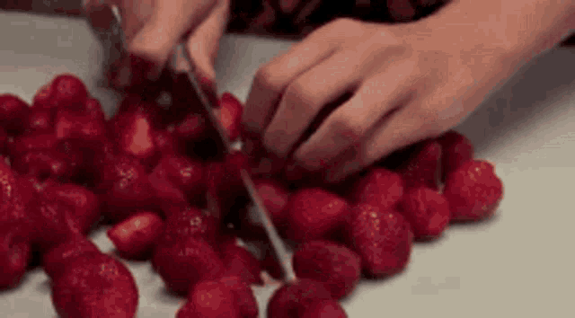 a woman is cutting strawberries with a knife on a cutting board .