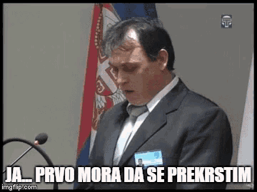 a man in a suit and tie is giving a speech in front of a microphone and a flag ..