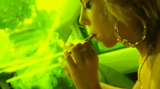 a woman is smoking a cigarette in a car in front of a green background .