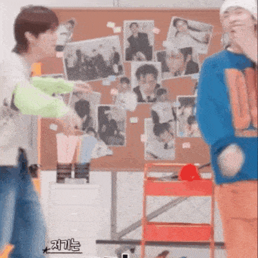 two men are standing next to each other in front of a bulletin board .
