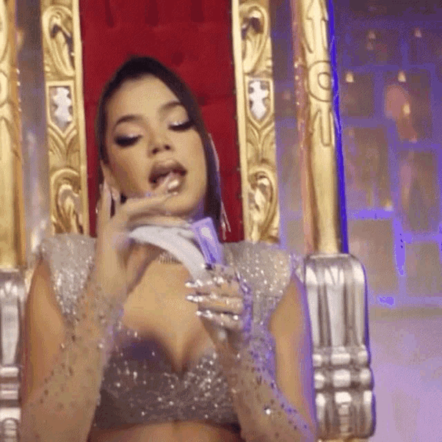 a woman in a silver dress is sitting on a throne holding a piece of paper in her mouth .