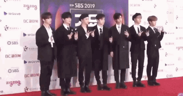 a group of young men standing on a red carpet giving peace signs .