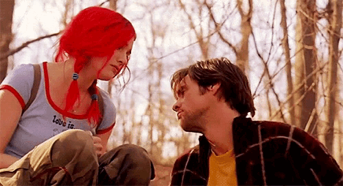 a man and a woman are looking at each other in the woods . the woman has red hair .