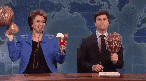 a man and a woman are sitting at a desk holding a drink and a drum .