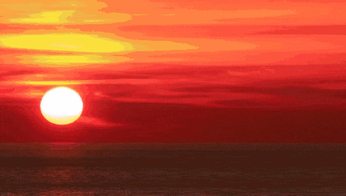 the sun is setting over the ocean with a red sky in the background