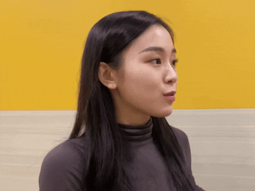 a woman with long black hair is making a surprised face in front of a yellow wall