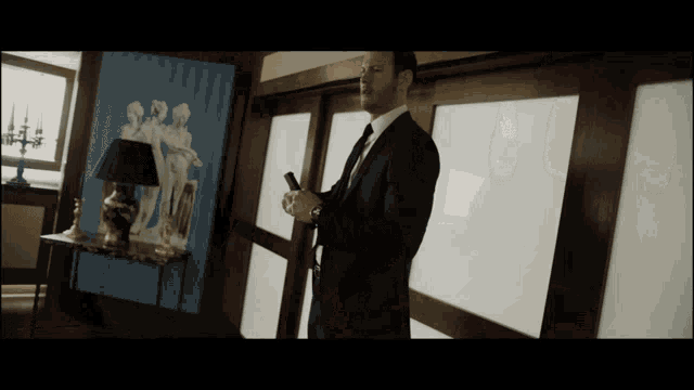 a man in a suit and tie is standing in a room with a lamp
