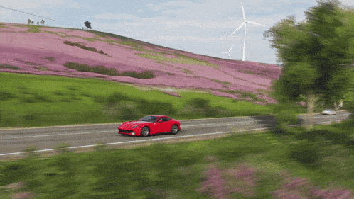 a red car is driving down a road in front of a hill with pink flowers